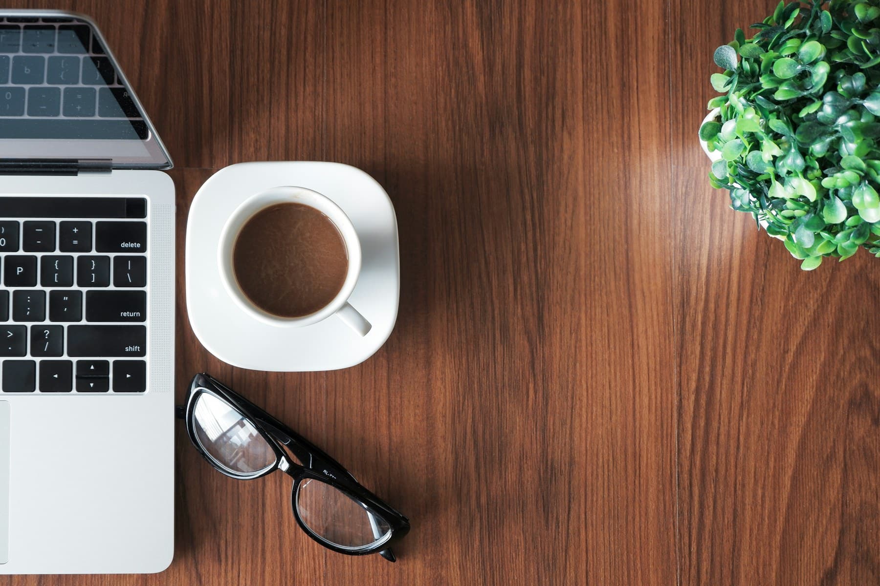 Laptop, Kaffee und eine Pflanze auf einem Holztisch