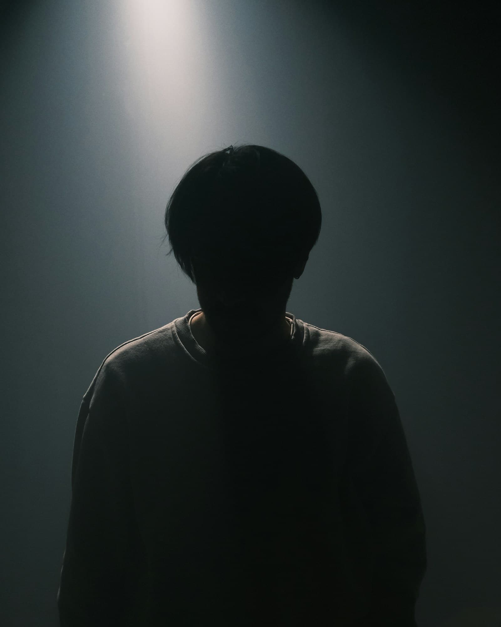 Platzhalterfoto: Silhouette einer Person, von einer einzelnen Lichtquelle im dunklen Raum beleuchtet